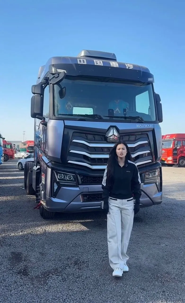 Used HOWO tractor truck parked in HebeiCar export yard in China — grey cab, fifth wheel coupling visible, other export stock in background